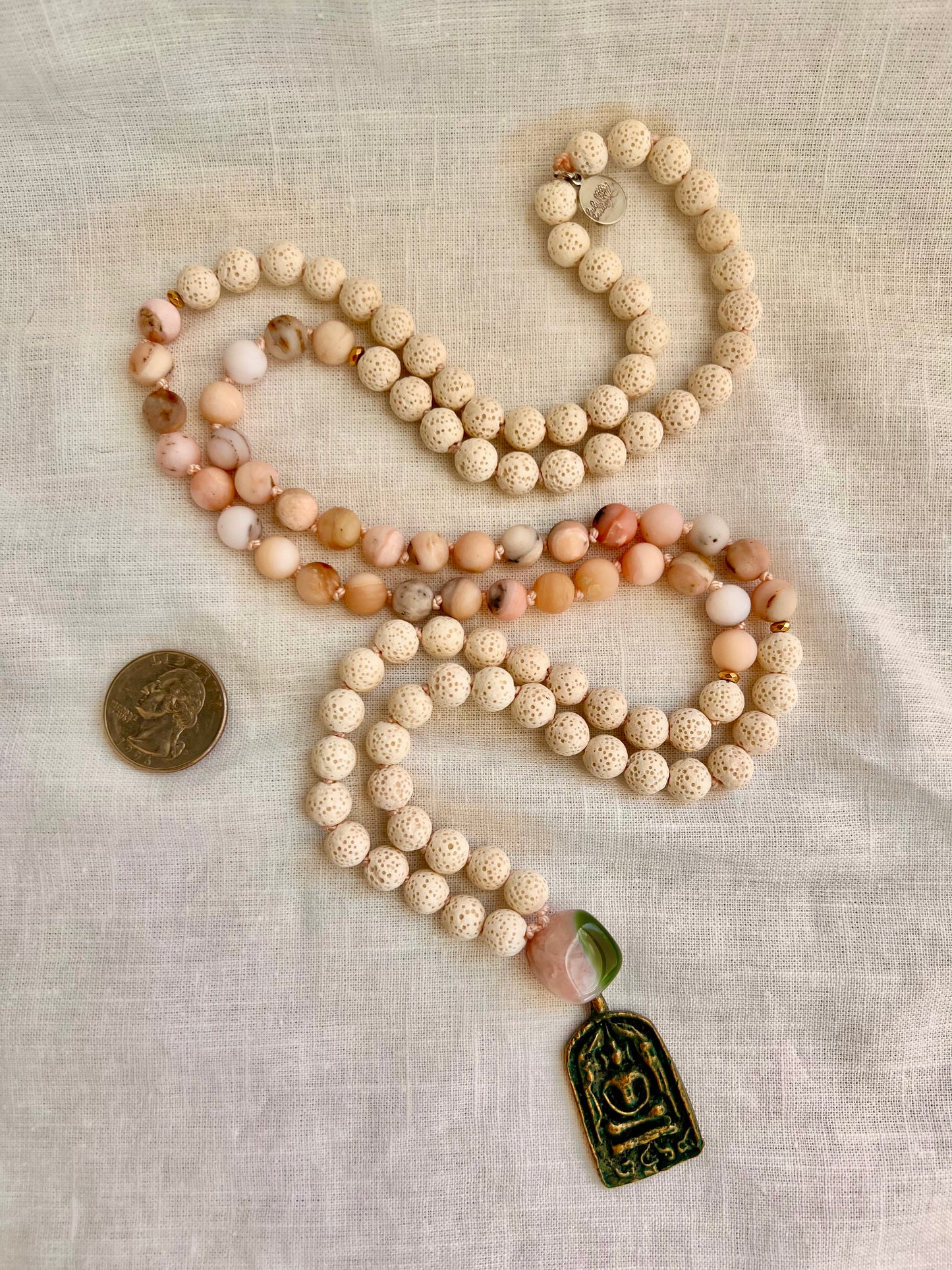 The Blooming Grace Mala necklace shown next to a quarter for scale, showing the full 108 bead length and Peruvian pink opal color variation