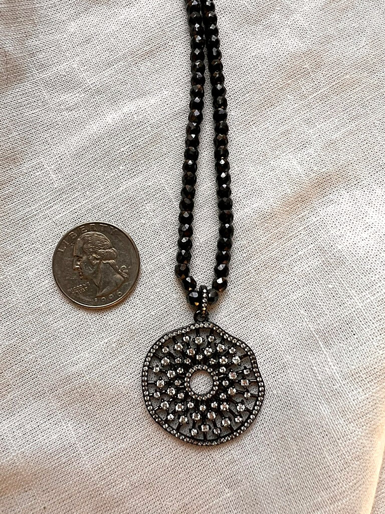 Midnight Mandala necklace next to a quarter for scale, showing the size of the 1.5 inch cubic zirconia medallion and faceted black zirconia beads