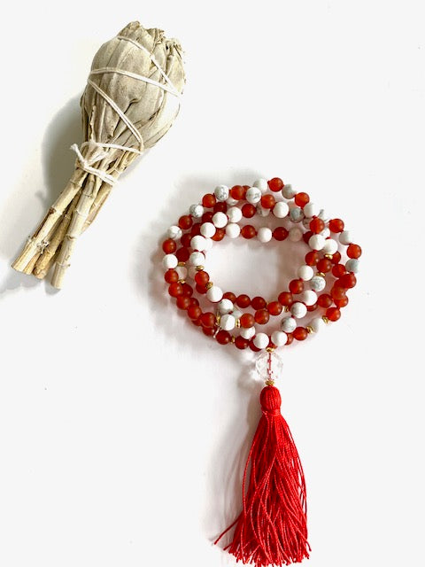 Coiled carnelian and howlite mala with a red silk tassel beside a white sage smudge bundle
