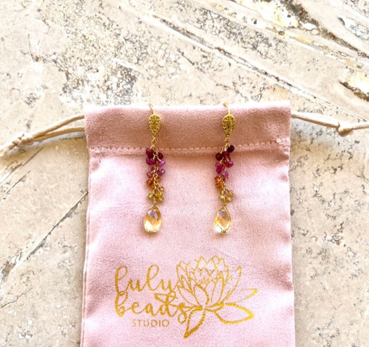 Ombre sapphire and citrine drop earrings laid on a blush pouch with the gold lotus logo