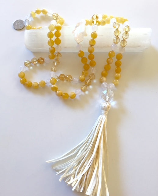 Yellow calcite and citrine mala with a cream leather tassel resting on a selenite stick, a US quarter above for scale
