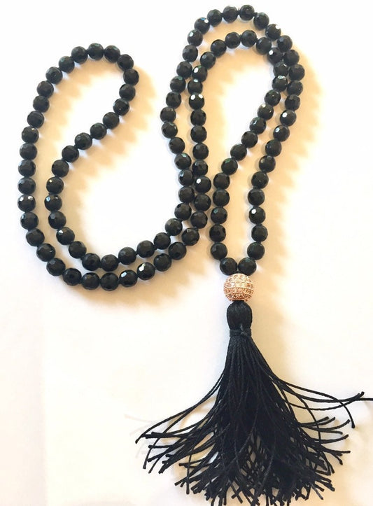 Faceted black onyx mala in an S curve with a long black tassel and a pave cubic zirconia guru bead