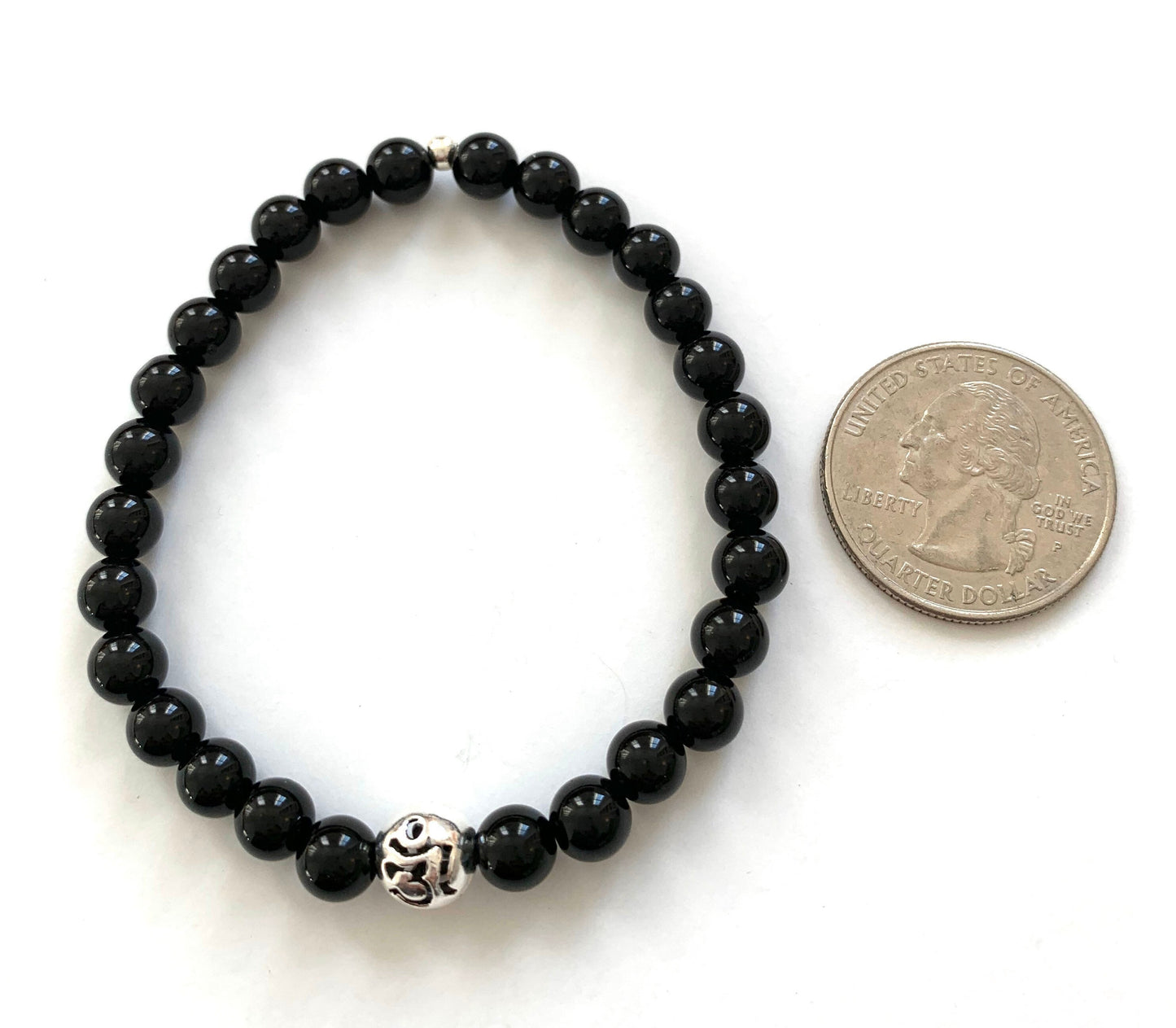 black onyx beaded bracelet with pierced sterling silver Om accent bead next to a quarter for size comparison