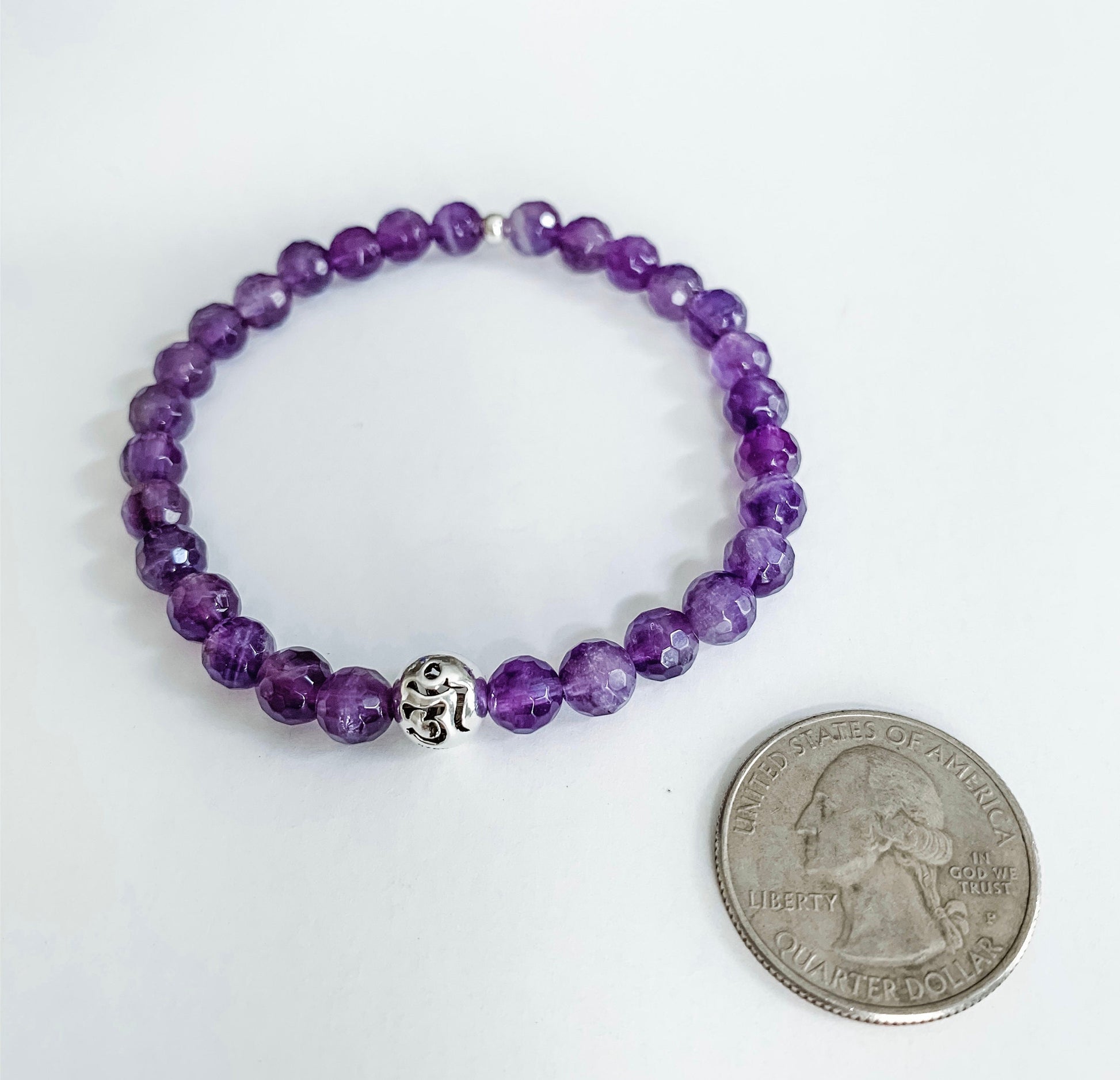 Amethyst beaded bracelet with sterling silver Om round ball bead charm next to a quarter for size comparison