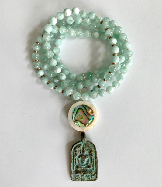 Coiled pale green angelite mala with an abalone and mother of pearl disc above a verdigris Buddha plaque pendant