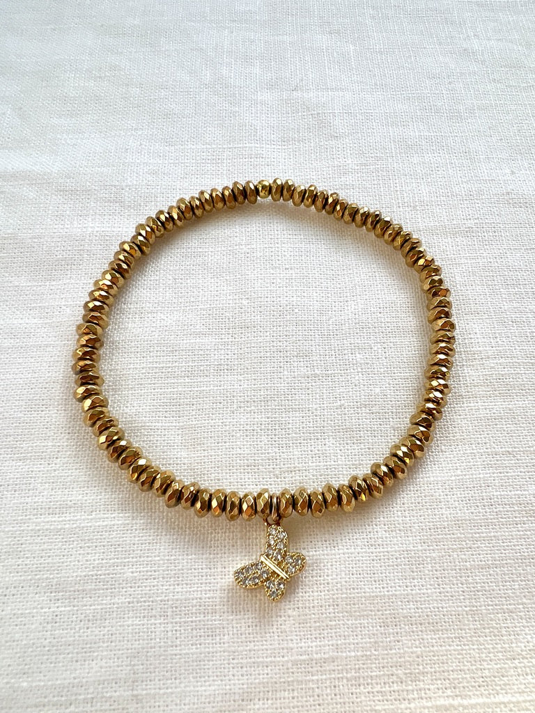 Butterfly Kisses bracelet of small faceted gold hematite beads with a pave cubic zirconia butterfly charm on cream linen