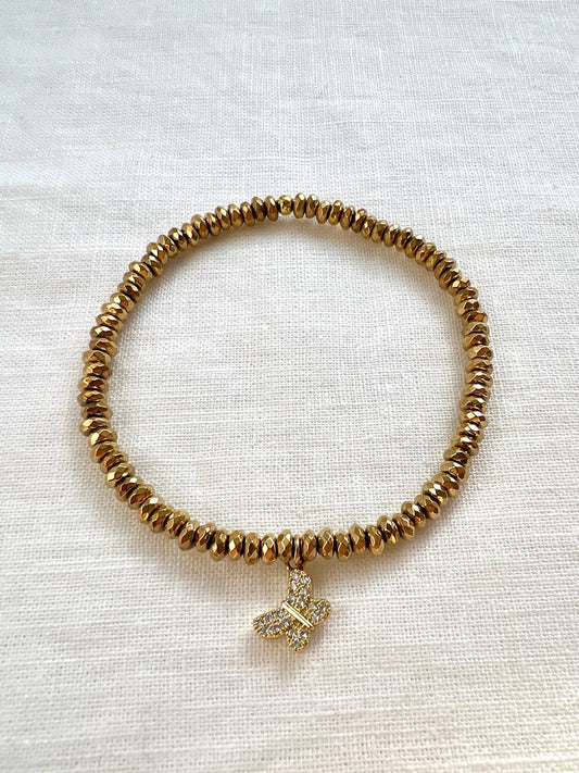 Butterfly Kisses bracelet of small faceted gold hematite beads with a pave cubic zirconia butterfly charm on cream linen