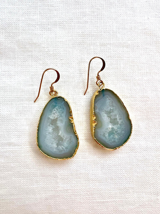 Pale green agate slice geode earrings edged in gold with white druzy centers, on cream linen