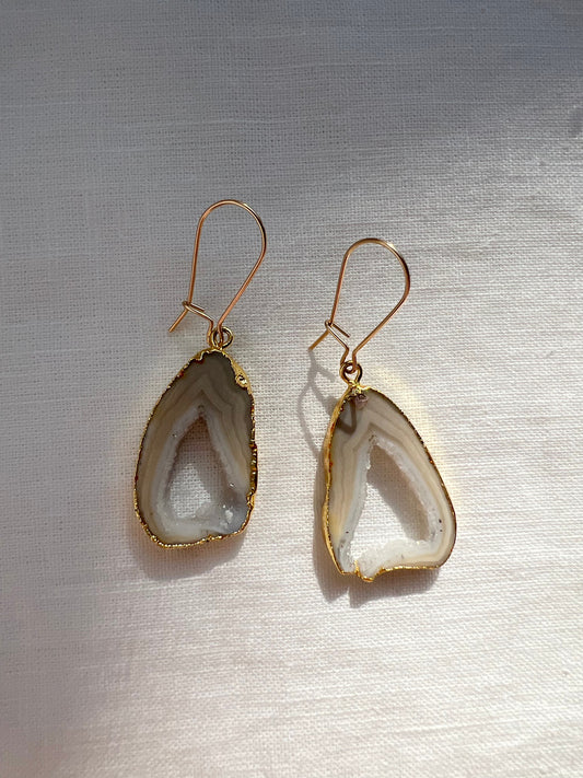 Grey open geode agate slice earrings edged in gold on long gold wires, on cream linen