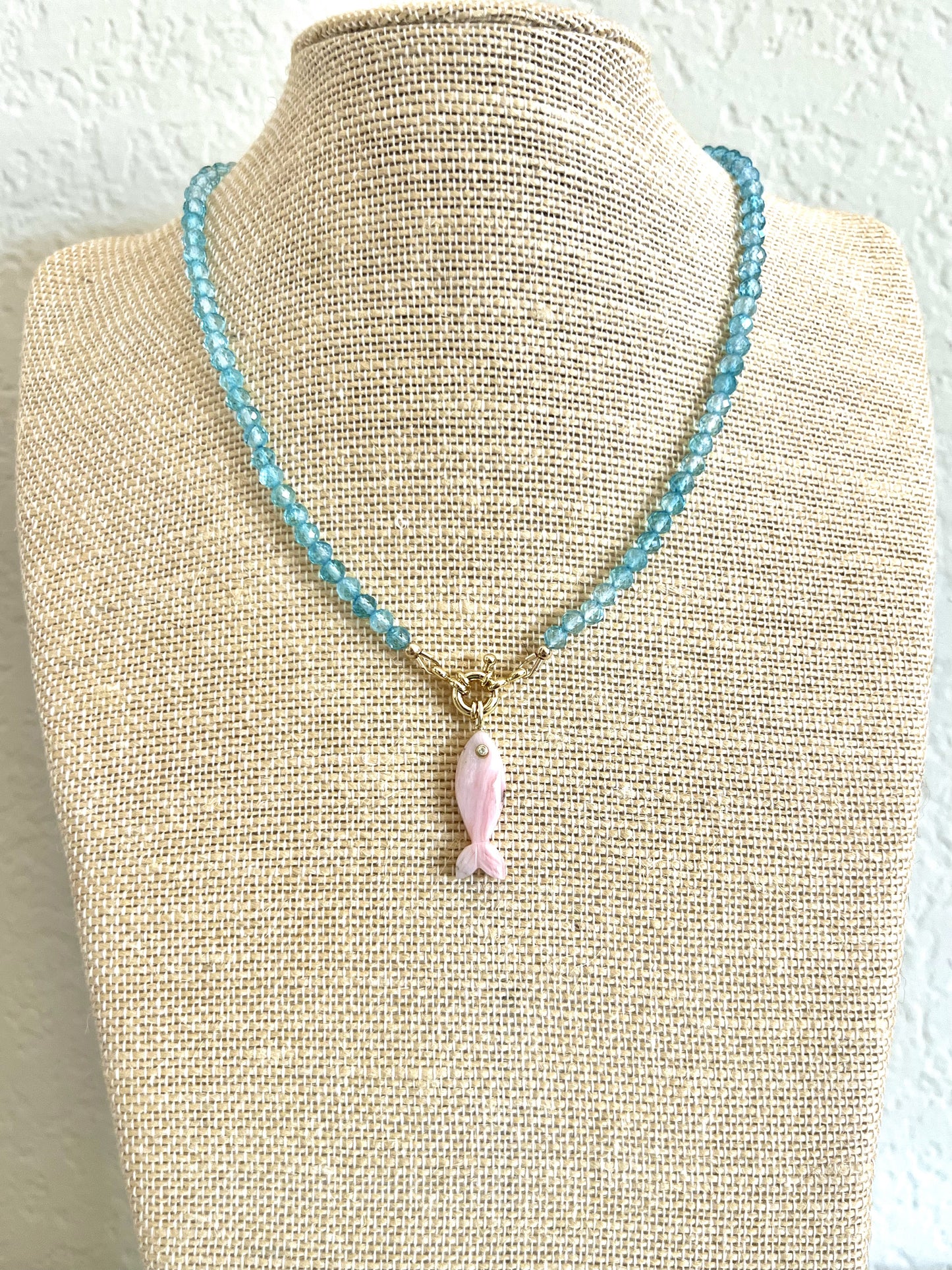 Blue topaz choker with a carved pink opal fish pendant displayed on a linen neck form