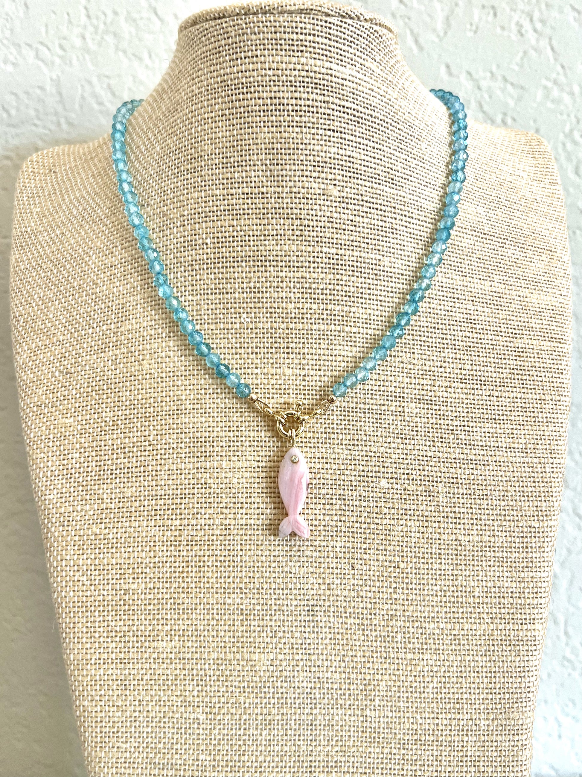 Blue topaz choker with a carved pink opal fish pendant displayed on a linen neck form