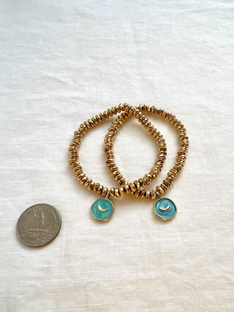 Two gold hematite angel wings charm bracelets beside a US quarter for size