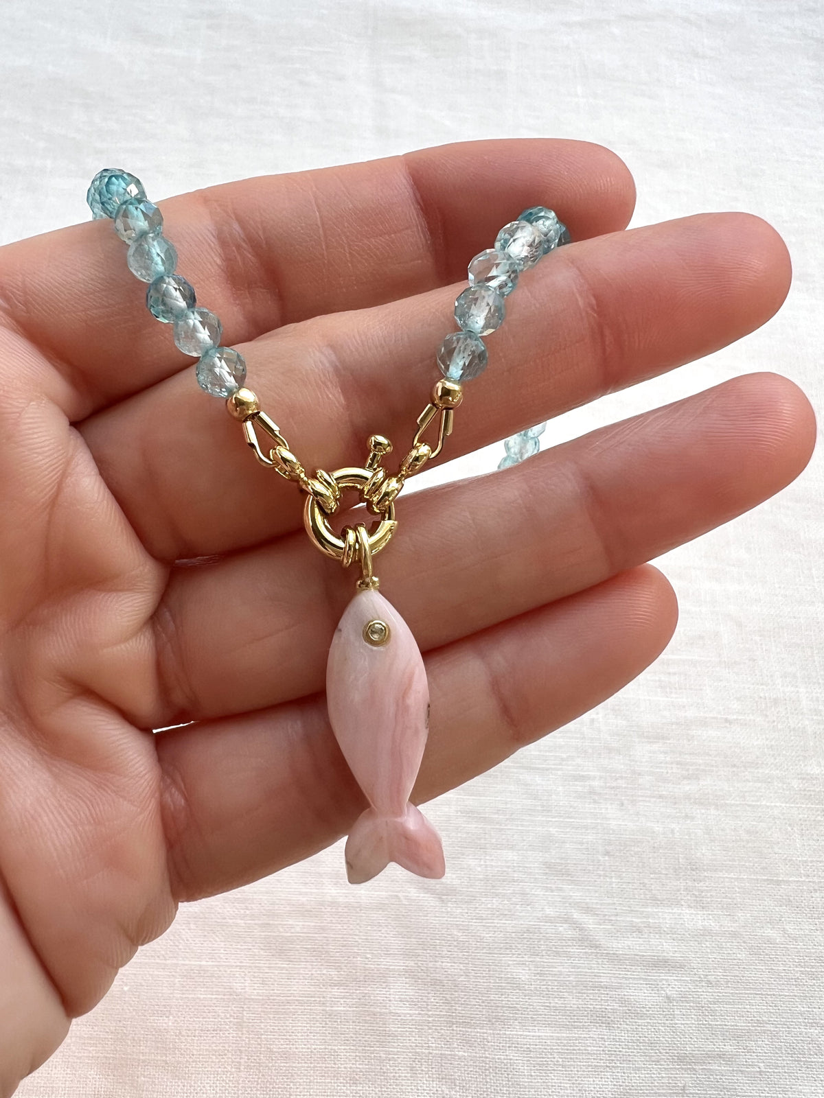 Blue topaz and carved pink opal fish necklace held in hand to show its size