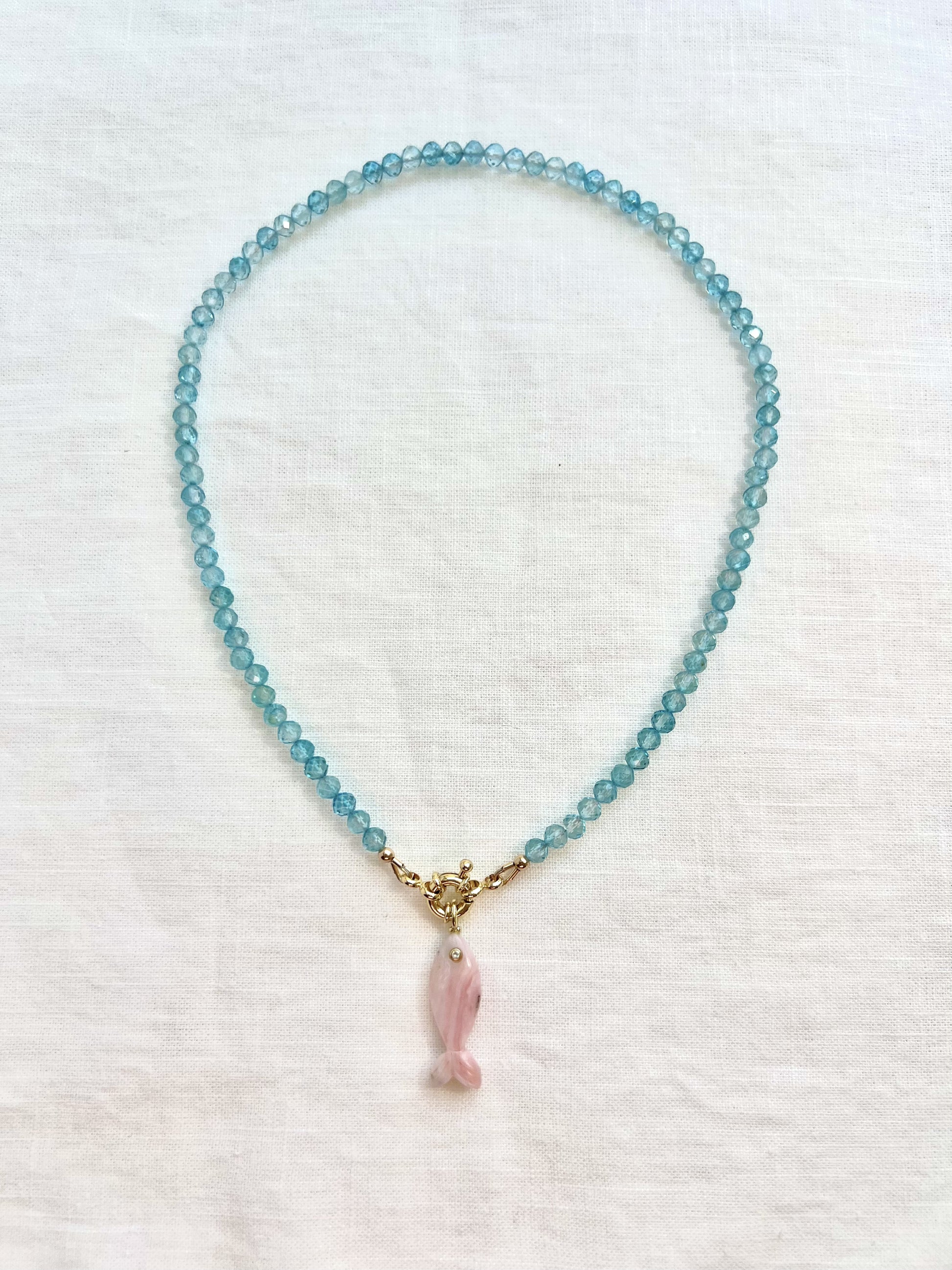 Full 16 inch blue topaz choker with a carved pink opal fish pendant, flat lay on white linen