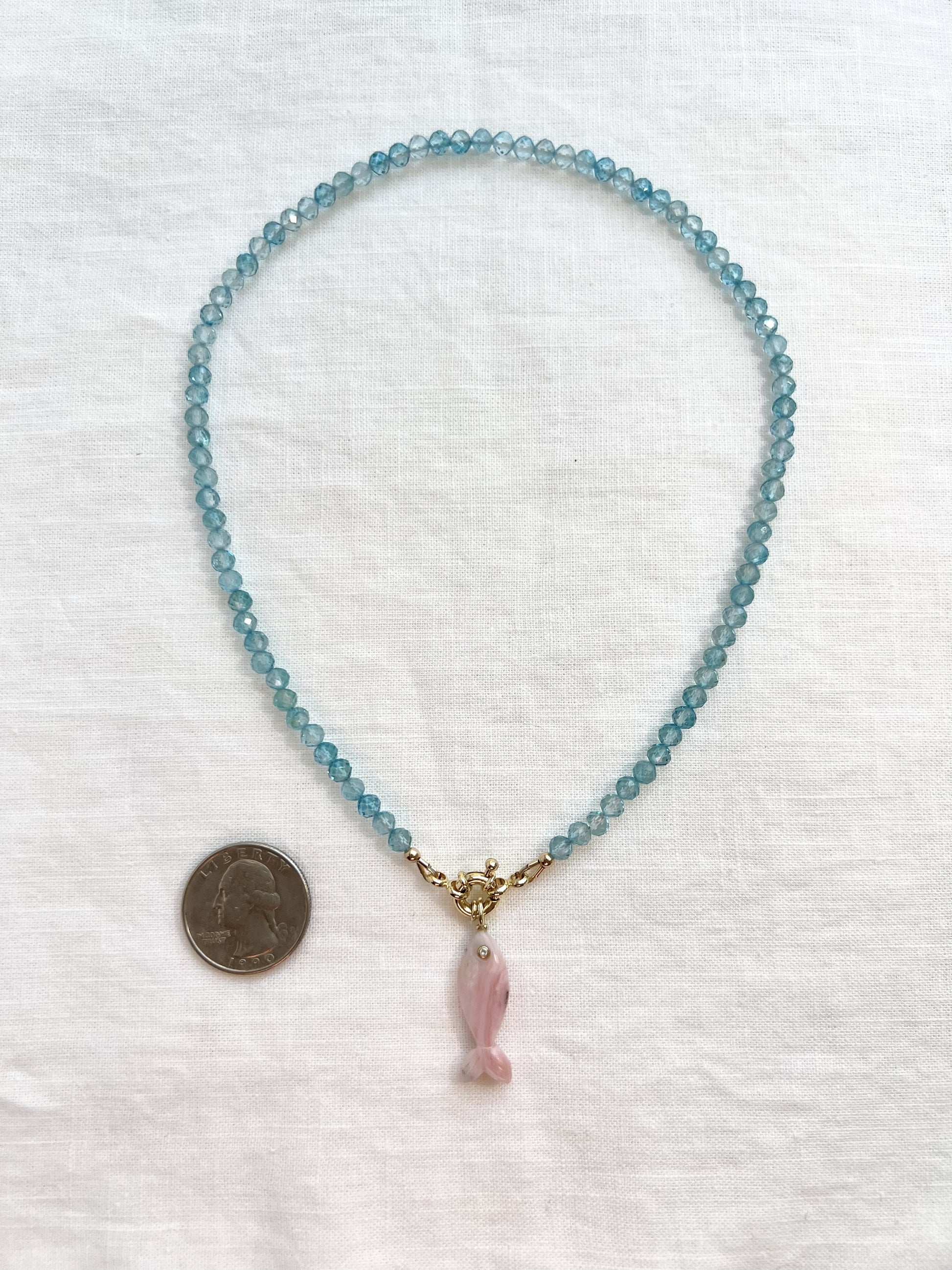 Blue topaz fish necklace laid flat beside a quarter for scale