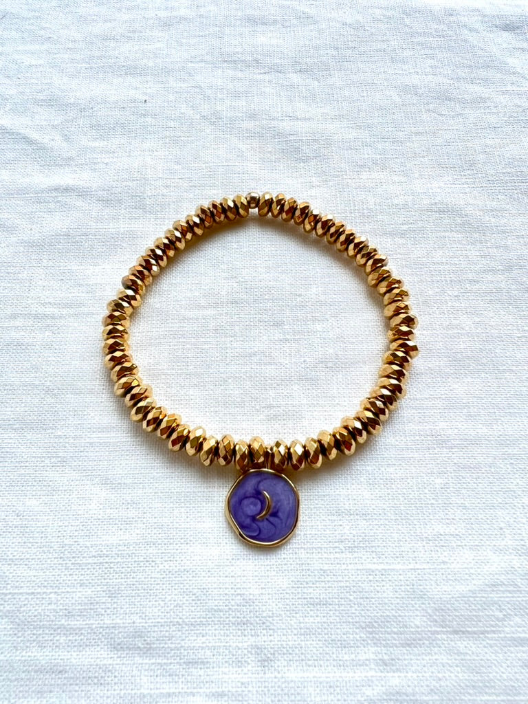 Purple enamel moon charm bracelet on faceted gold plated hematite beads, 7 inch stretch bracelet on white linen