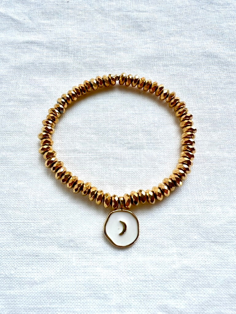 White enamel moon charm bracelet on faceted gold plated hematite beads, 7 inch stretch bracelet on white linen