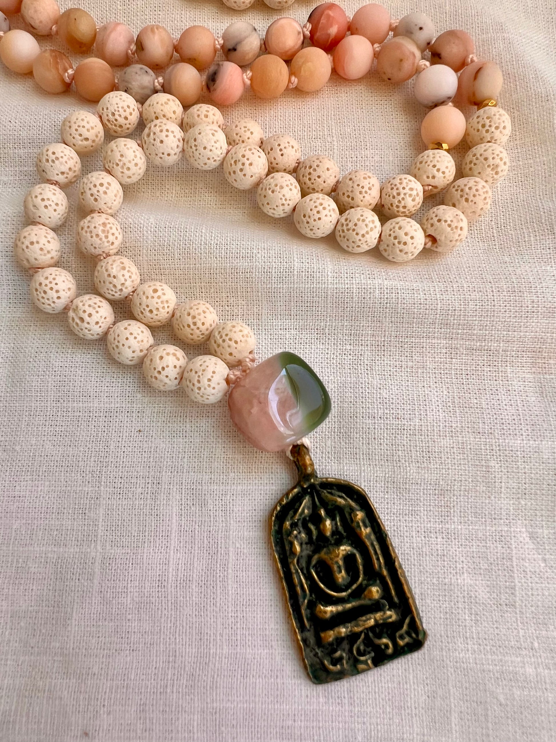 Close up of the pink and green banded agate guru bead and antique patina brass Buddha amulet pendant on the Blooming Grace Mala