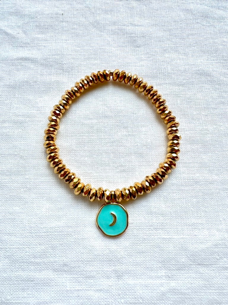 Turquoise enamel moon charm bracelet on faceted gold plated hematite beads, 7 inch stretch bracelet on white linen