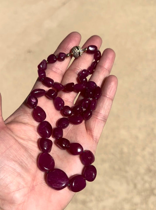 Deep red ruby nugget necklace held in an open hand, showing its length and the pave magnetic clasp