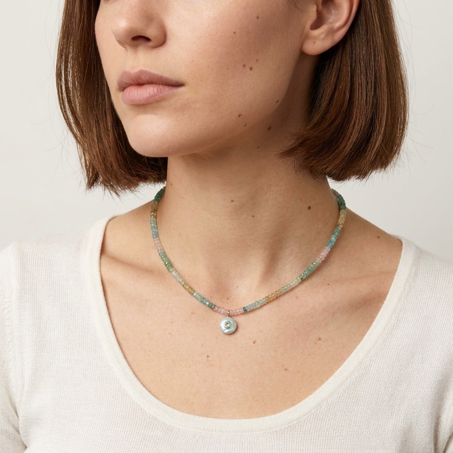 Woman wearing the larimar necklace with a cream top, pastel aquamarine and morganite beads with the pale blue larimar pendant at the collarbone