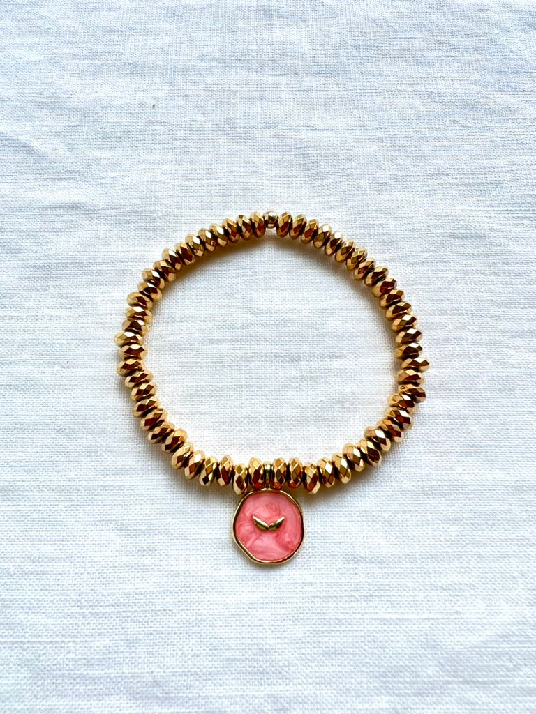 Pink enamel angel wing charm bracelet on faceted gold plated hematite beads, 7 inch stretch bracelet on white linen
