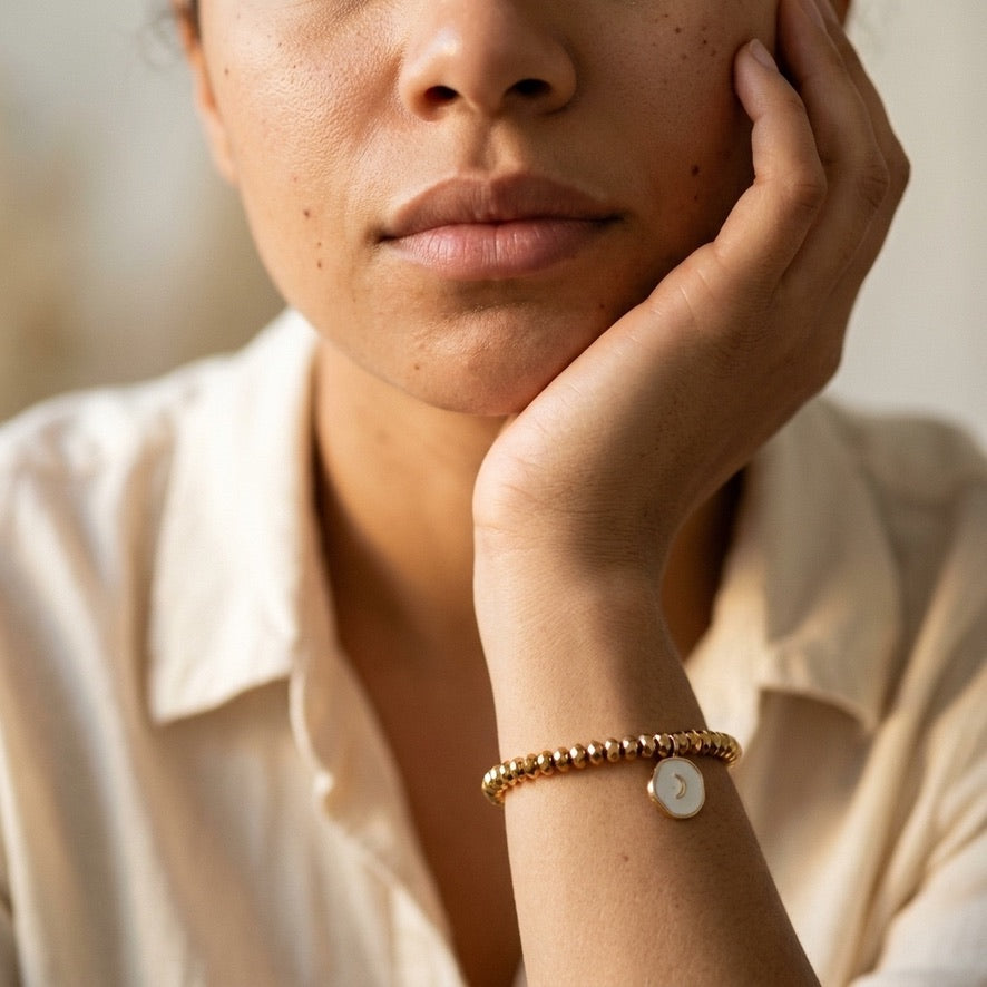 Woman wearing the white enamel moon charm bracelet on her wrist, gold plated hematite stretch bracelet