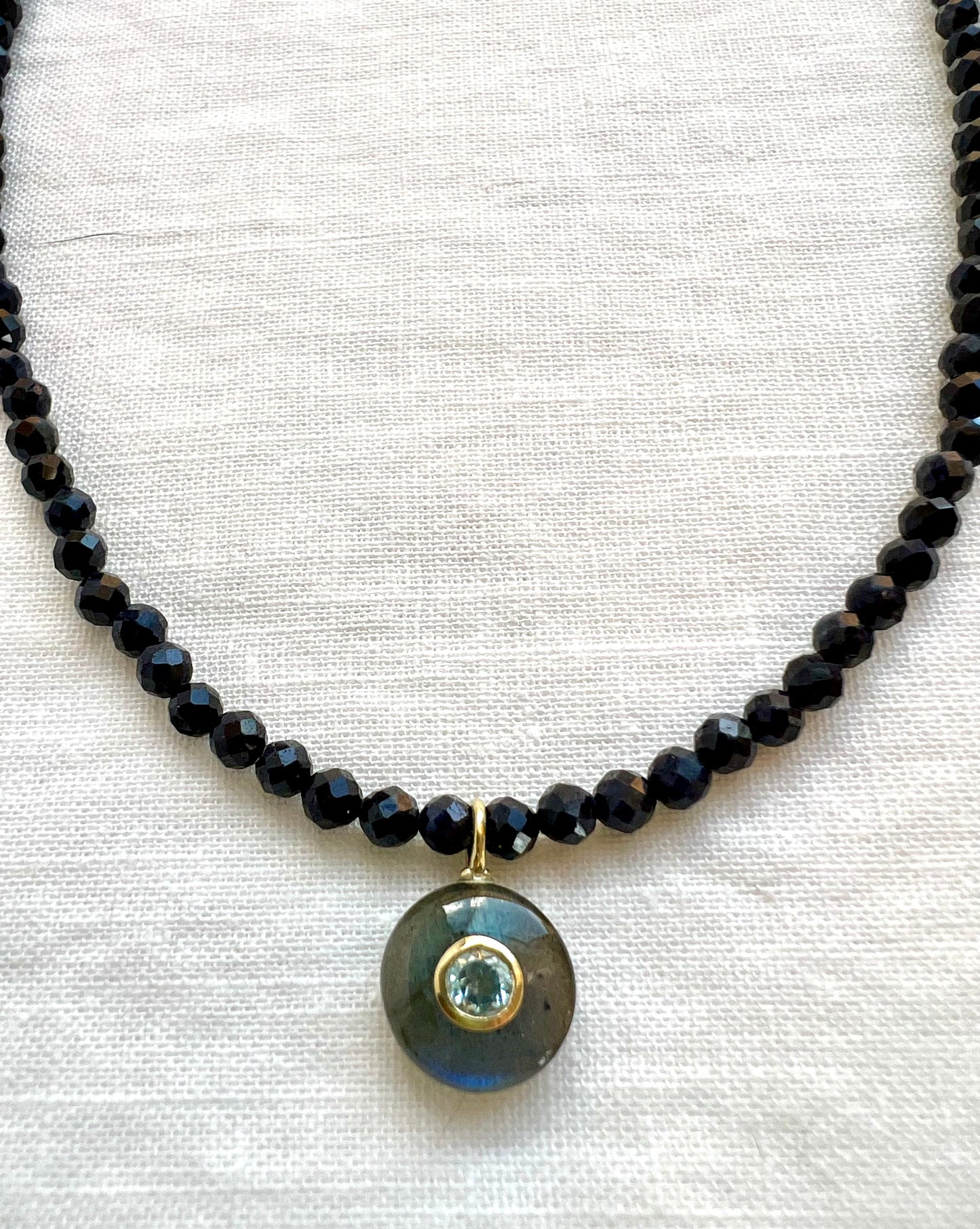 Labradorite pendant with a bezel set blue topaz hanging from a strand of faceted blue sapphire beads