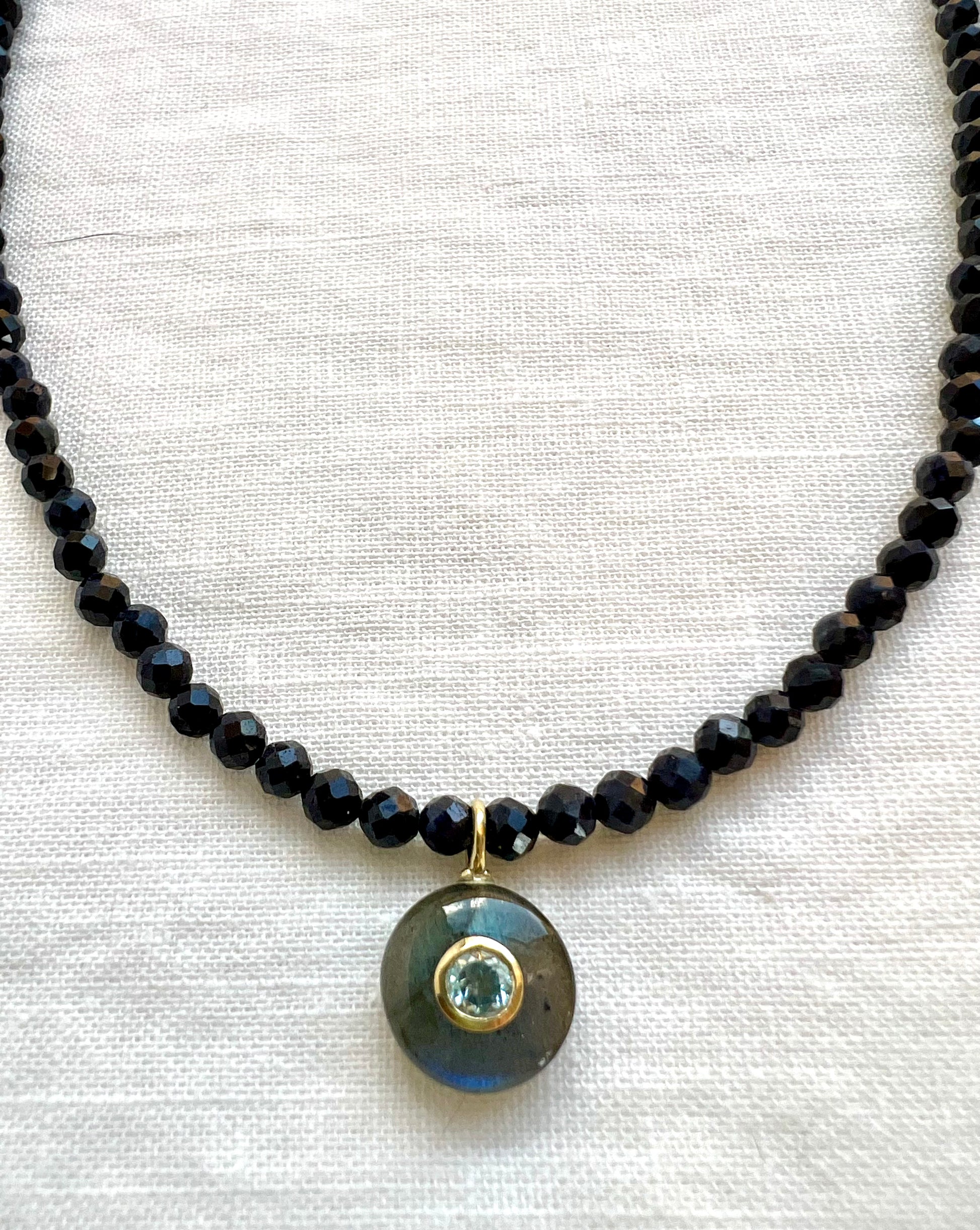 Labradorite pendant with a bezel set blue topaz hanging from a strand of faceted blue sapphire beads