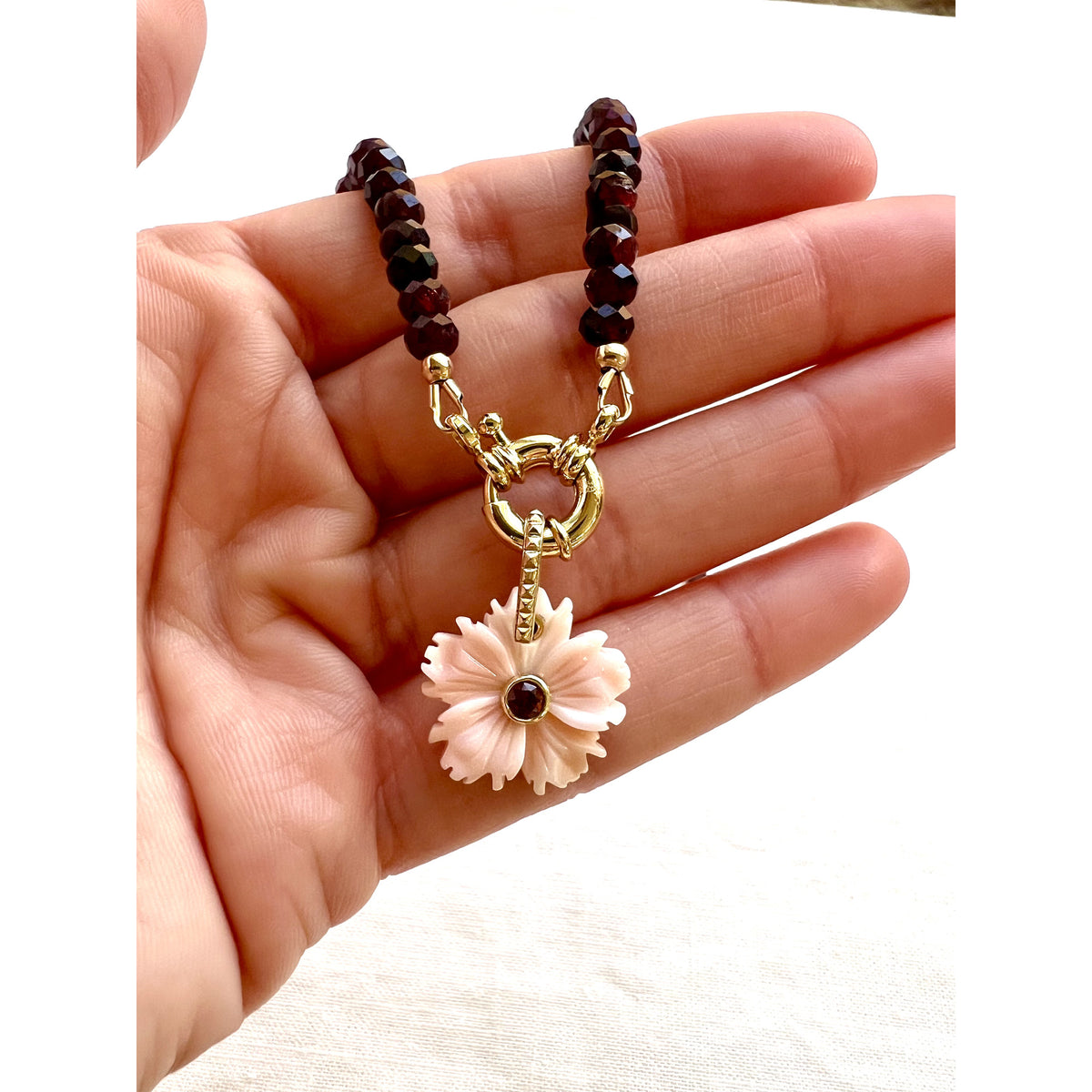 Garnet and carved shell flower choker necklace held in a hand to show its size