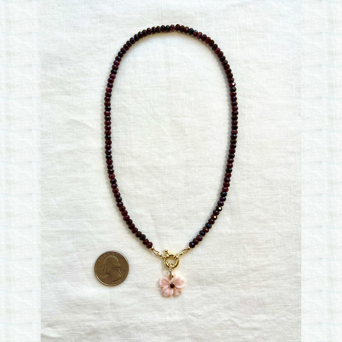 Garnet choker necklace laid flat beside a quarter for scale, the carved shell flower slightly smaller than the coin