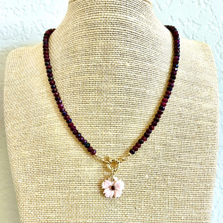 Garnet choker necklace with its pink shell flower pendant displayed on a linen neck form
