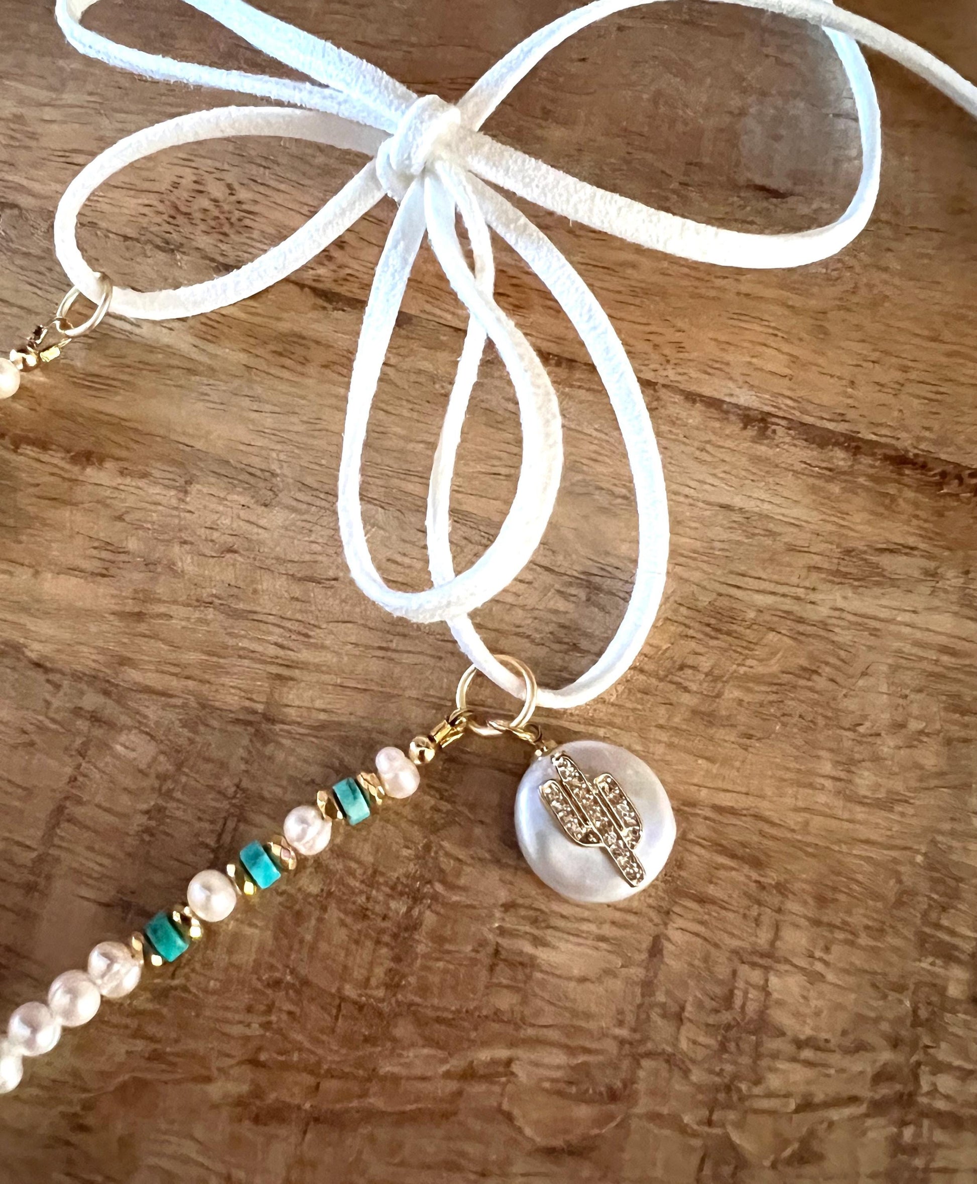 Close view of the adjustable suede ties knotted in a bow, with the pave cactus charm on a freshwater pearl drop hanging below.