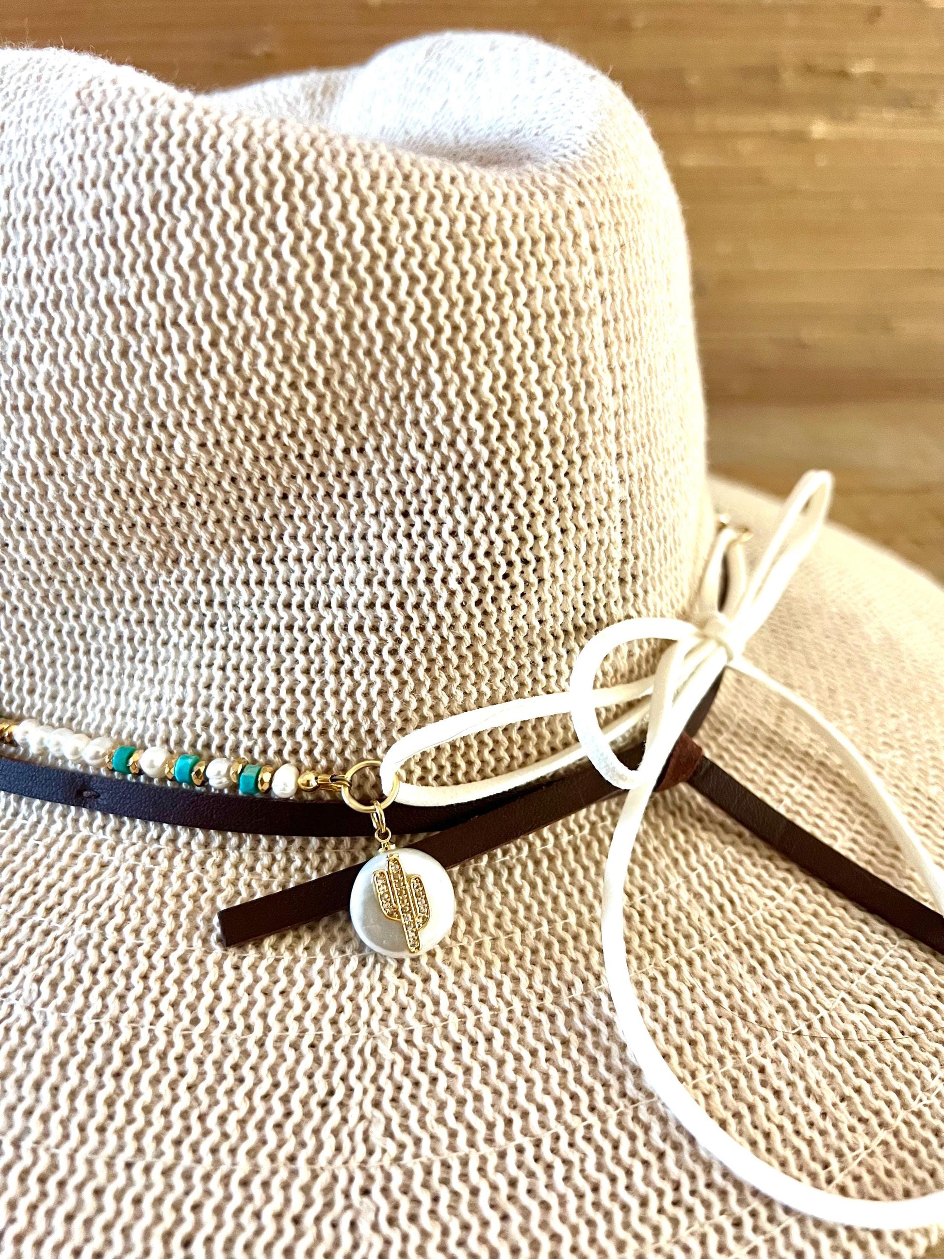 Arizona turquoise and freshwater pearl beaded hat band tied around the crown of a natural straw sun hat, finished with a gold cactus charm and a dark suede tie.