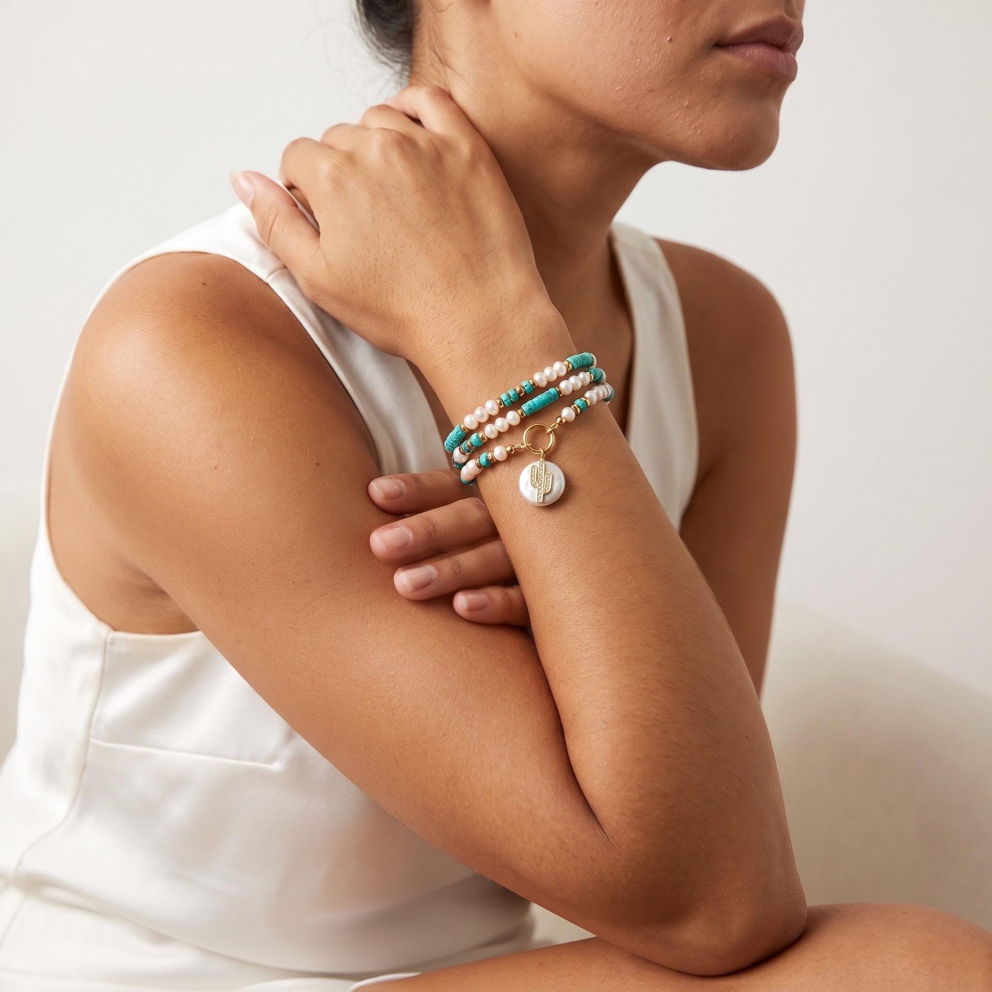 Turquoise and pearl strand wrapped twice around a wrist as a bracelet, stacked with gold bangles.