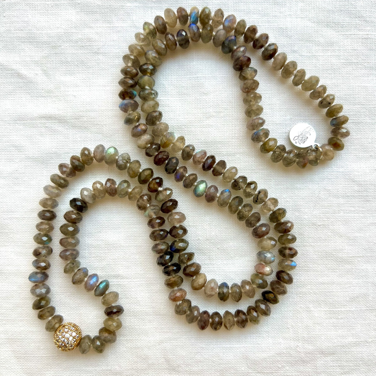 Full Emberlight mala necklace of faceted labradorite with a gold plated pave guru bead, coiled on white linen