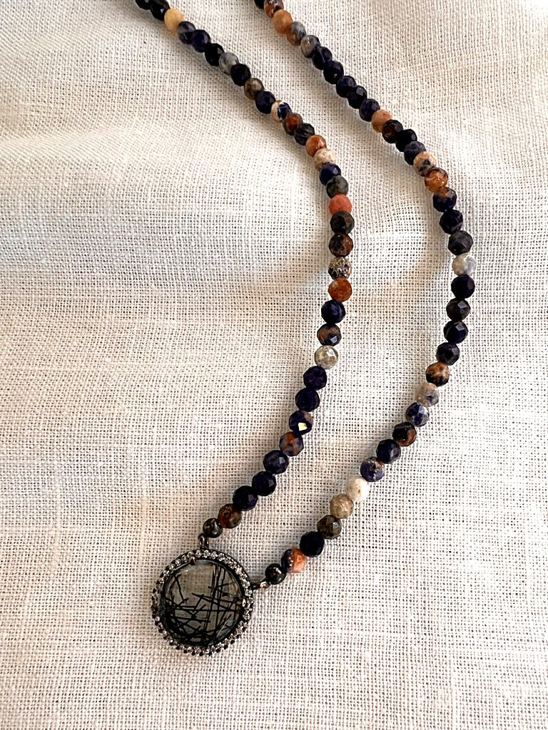Close up of the natural rutilated quartz pendant laced with dark needles and encircled by a halo of cubic zirconia, hanging from faceted sodalite beads