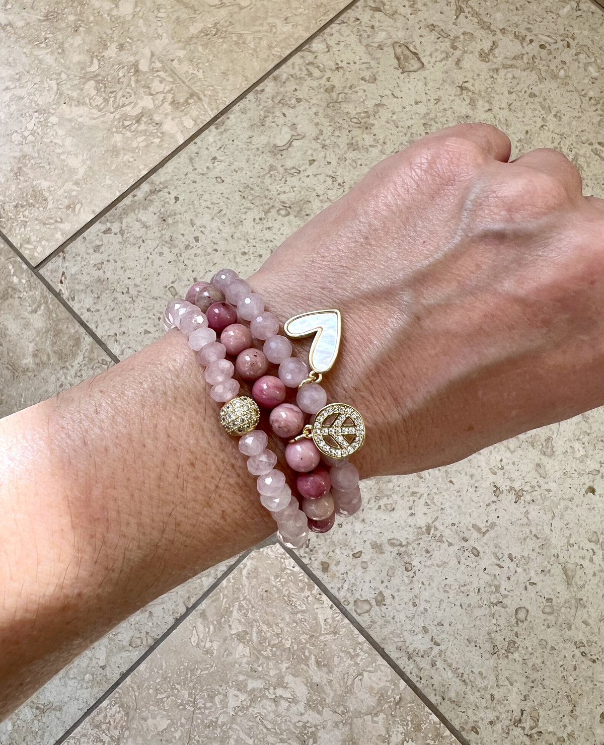 All three Peace and Love bracelets worn stacked on a wrist, rose quartz and rhodonite with gold peace and heart charms