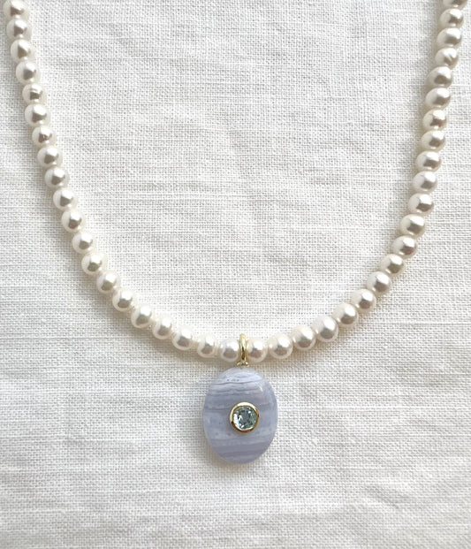 Freshwater pearl choker with a blue lace agate pendant set with a bezel set blue topaz, close view on white linen