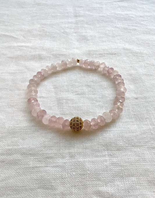Faceted rose quartz rondelle stretch bracelet with a single gold plated pave CZ bead, laid flat on white linen