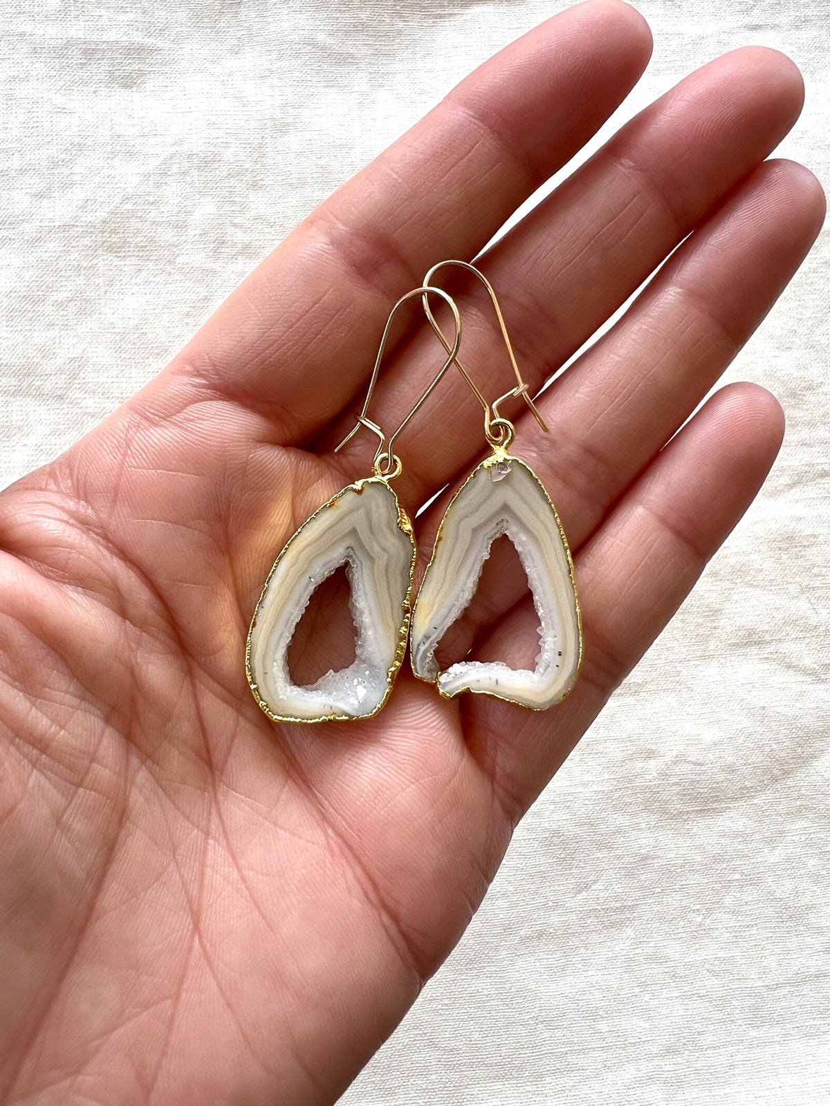 Grey open geode agate slice earrings held in an open palm, showing how large the slices are