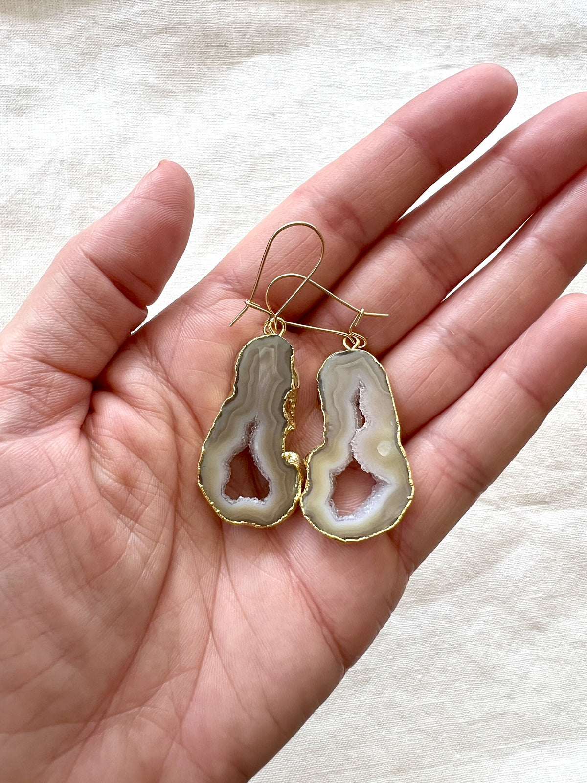 Cream and beige agate slice geode earrings held in an open palm, showing how large the slices are