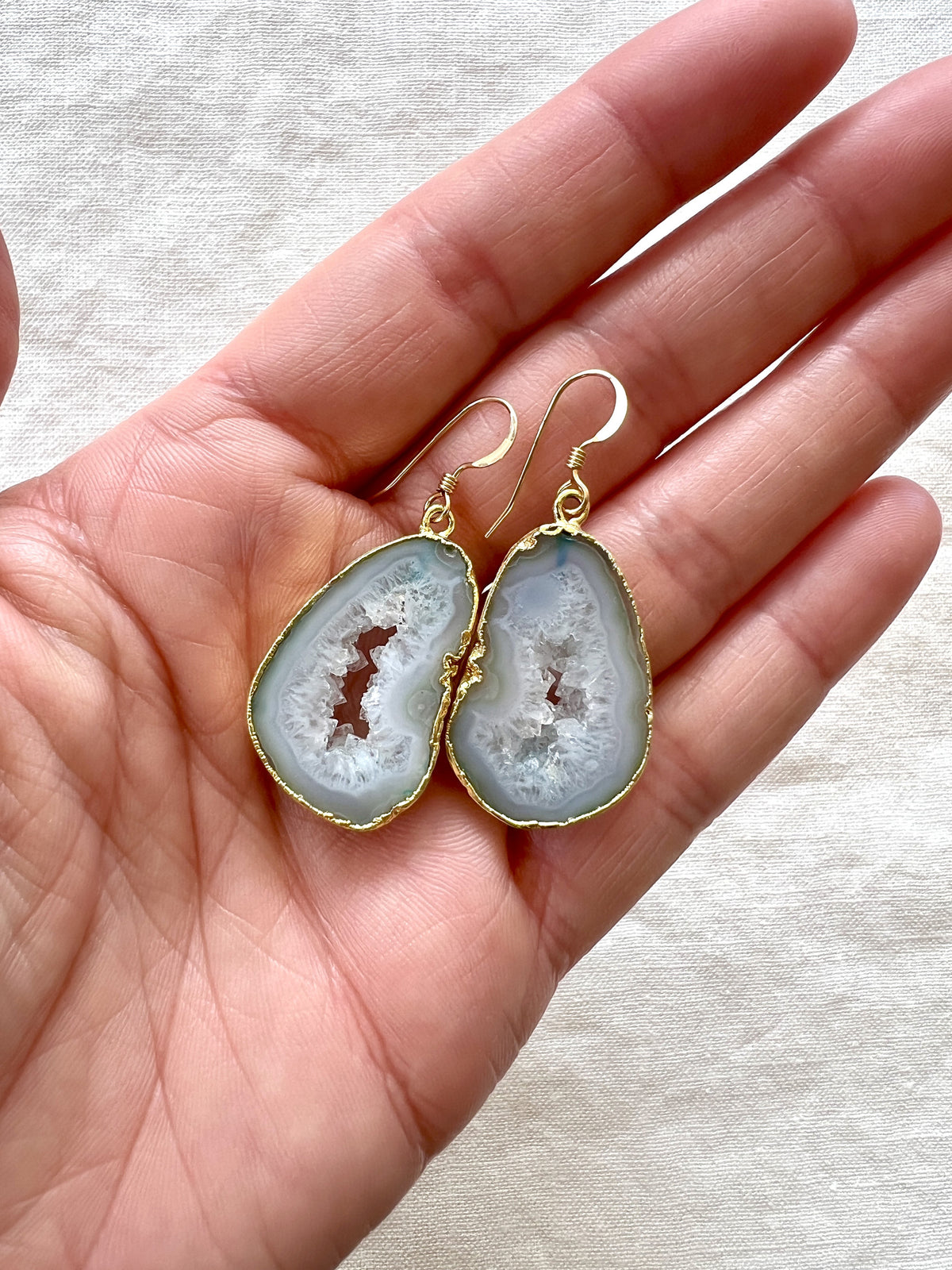 Pale green agate slice geode earrings held in an open palm, showing how large the slices are