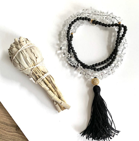 Tassel necklace with clear quartz and black lava beads, pave cz gold plated guru bead, black silk tassel, pictured next to a sage bundle