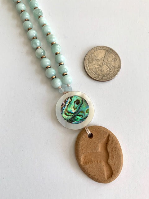 green Angelite mala beads close up the mother of pearl guru bead and oil diffuser hummingbird terracotta pendant next to a quarter for size comparison