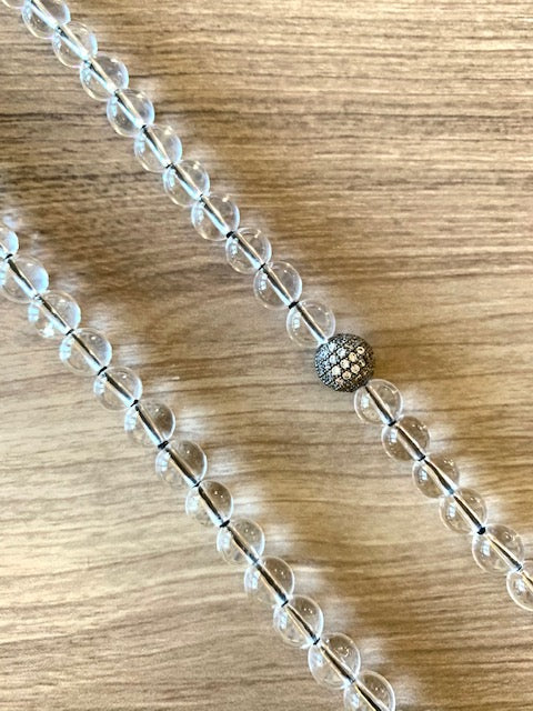 close up of clear crystal quartz mala beads, 8mm, knotted on black nylon thread.  CZ  Guru bead