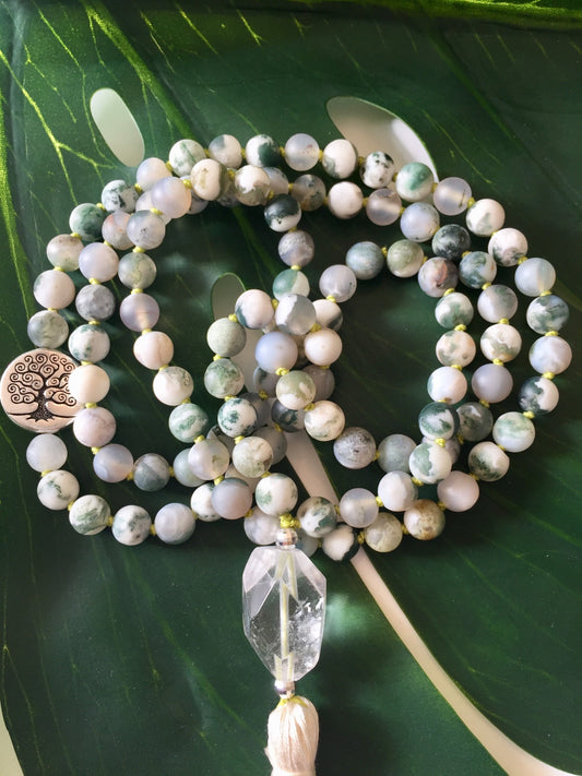 Tree agate mala coiled on a monstera leaf with a faceted quartz guru bead and a silver tree of life charm