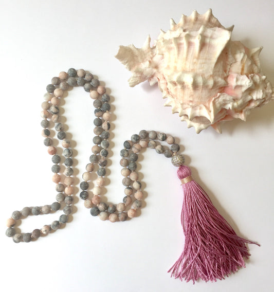 Pink zebra jasper mala in an S curve with a dusty rose tassel beside a spiny conch shell
