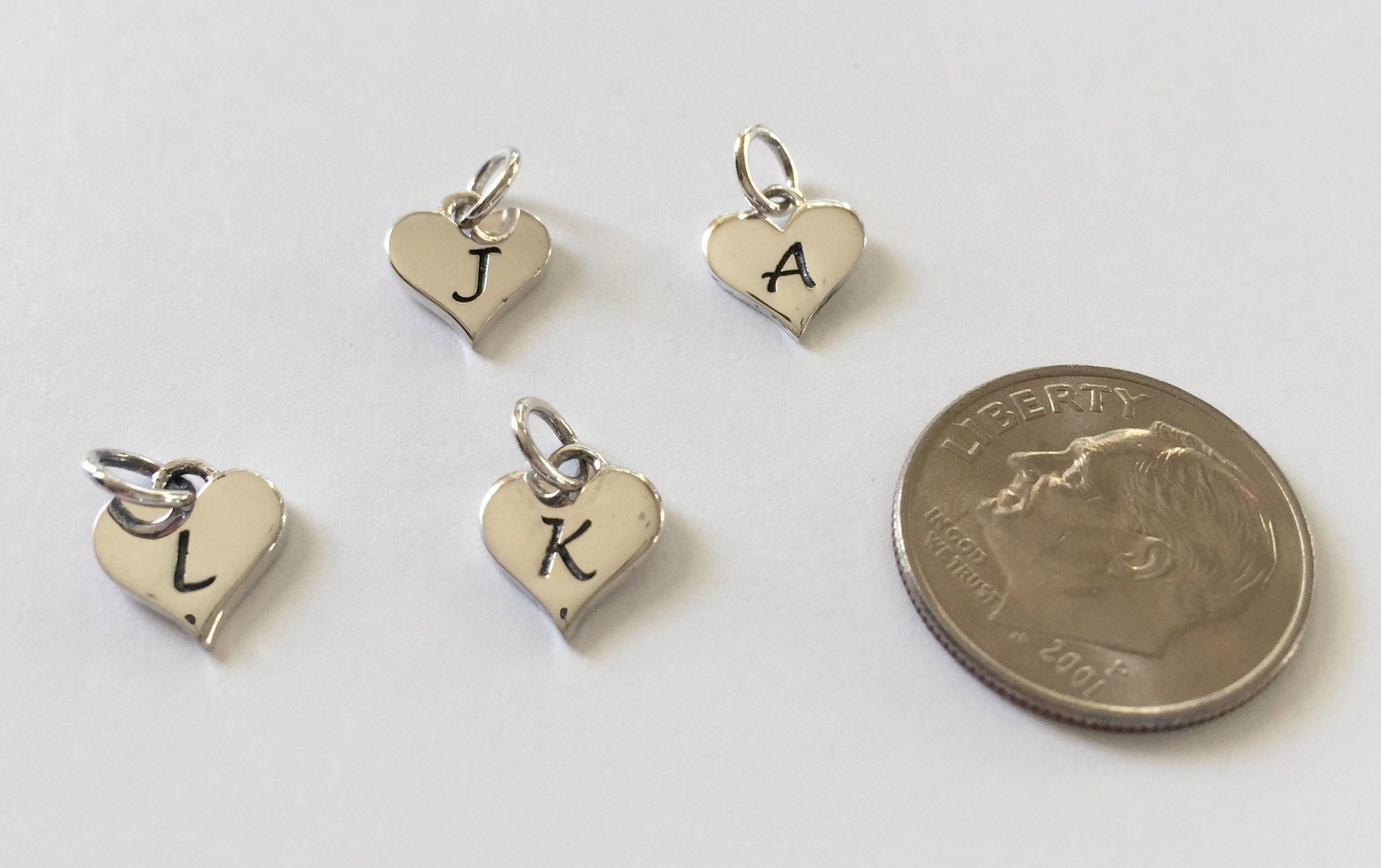 sterling silver heart shaped initial charms next to a  dime for size comparison