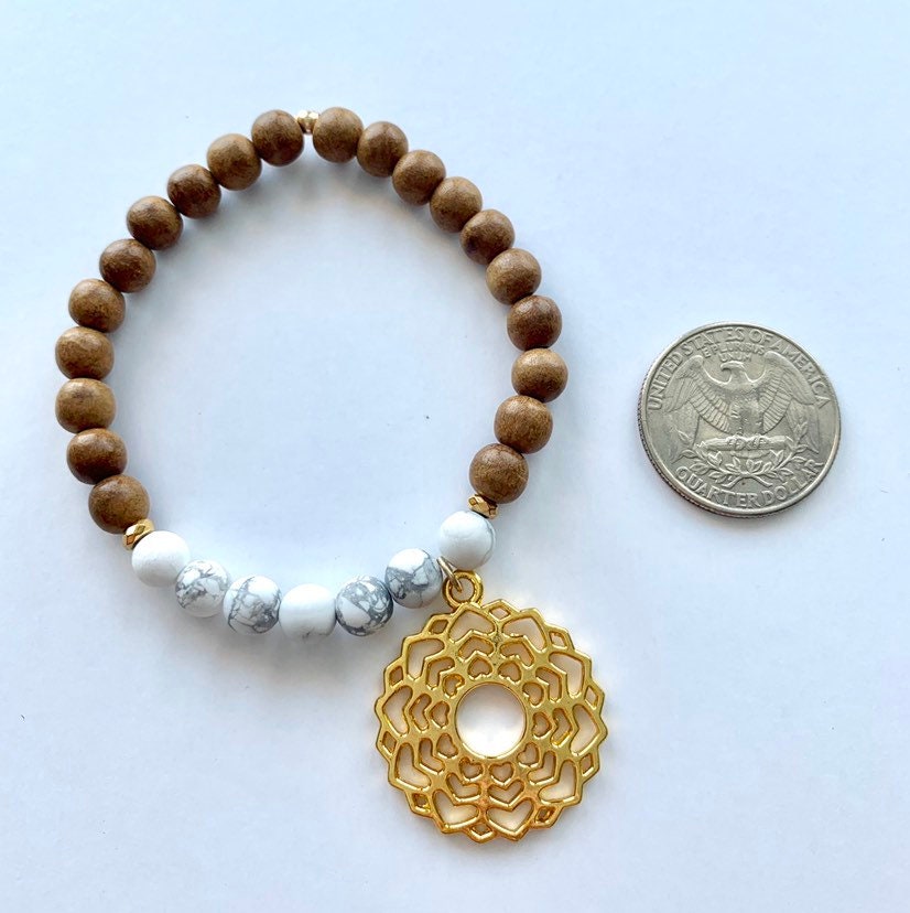 Sandalwood and howlite jasper bracelet with gold toned crown chakra charm, strung on stretch cord next to a quarter for size comparison